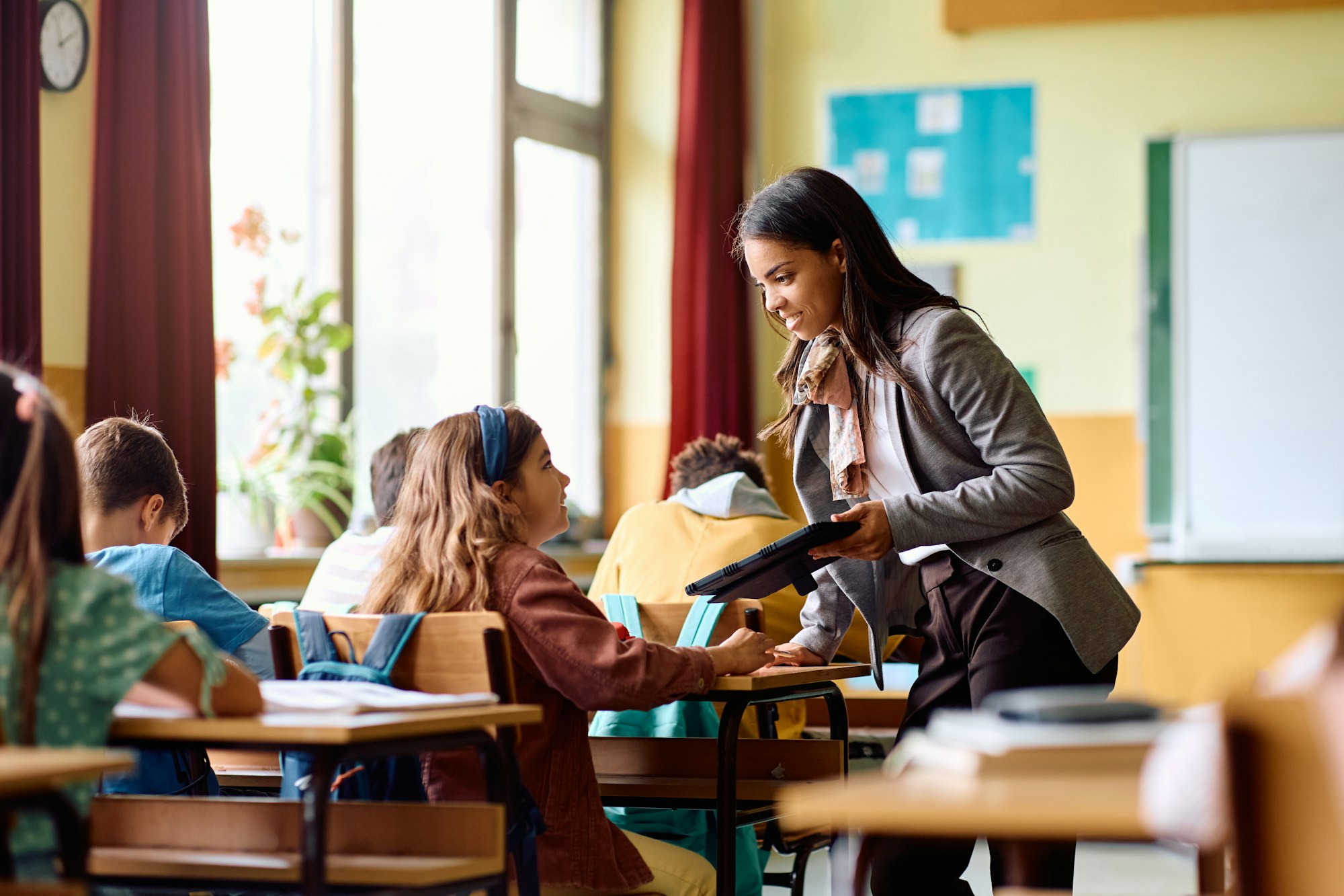 Happy Hispanic teacher and schoolgirl talking during a class in the classroom.